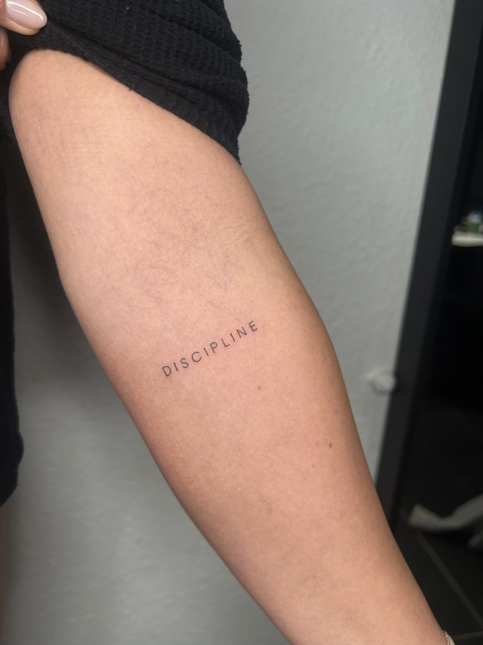 Schriftzug „DISCIPLINE“ mit feinen, weit gesetzten Großbuchstaben am Oberarm.
