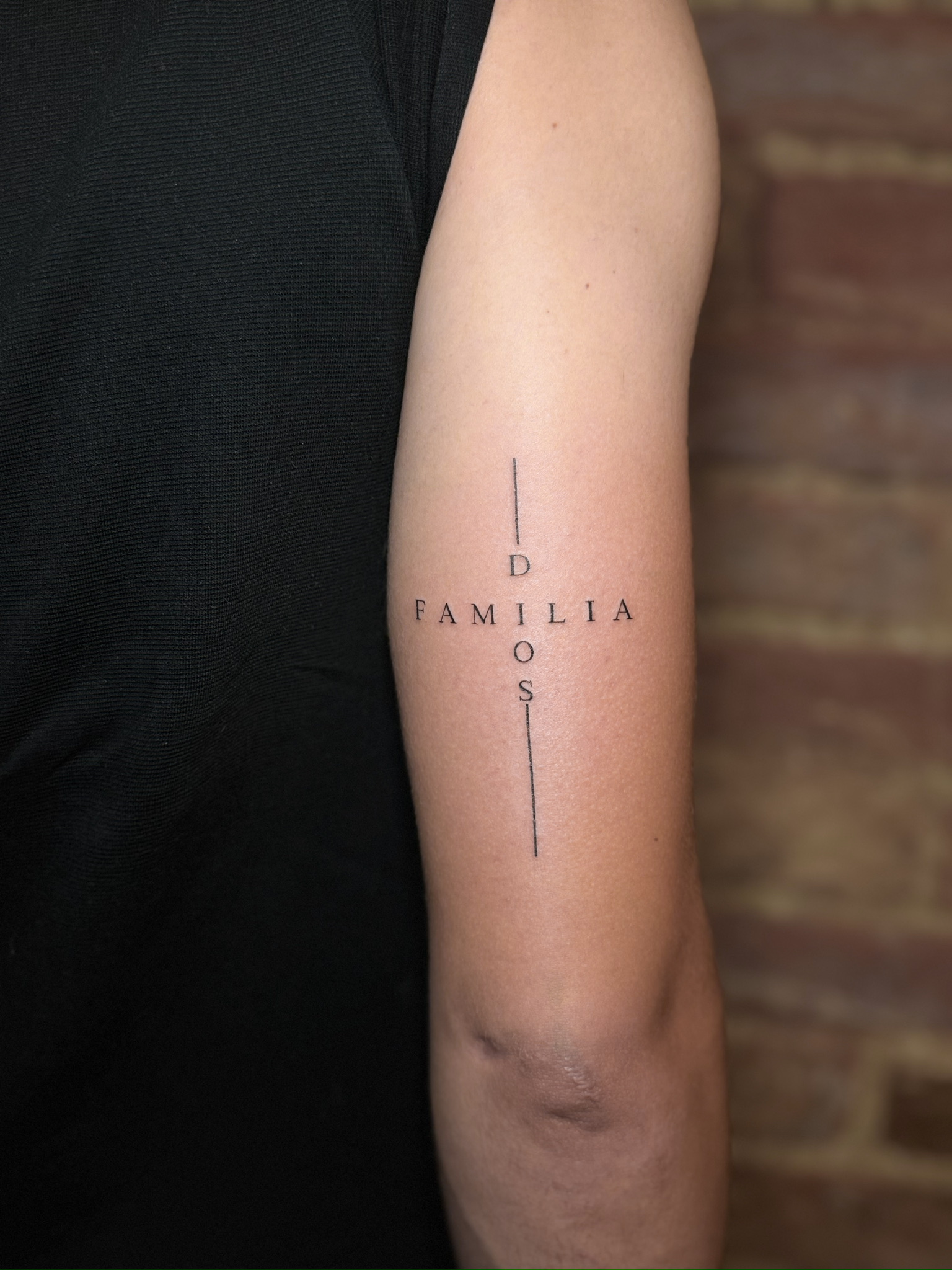 „FAMILIA“ und „DIOS“ als sich kreuzende Schriftzüge mit feinen Linien am Arm.