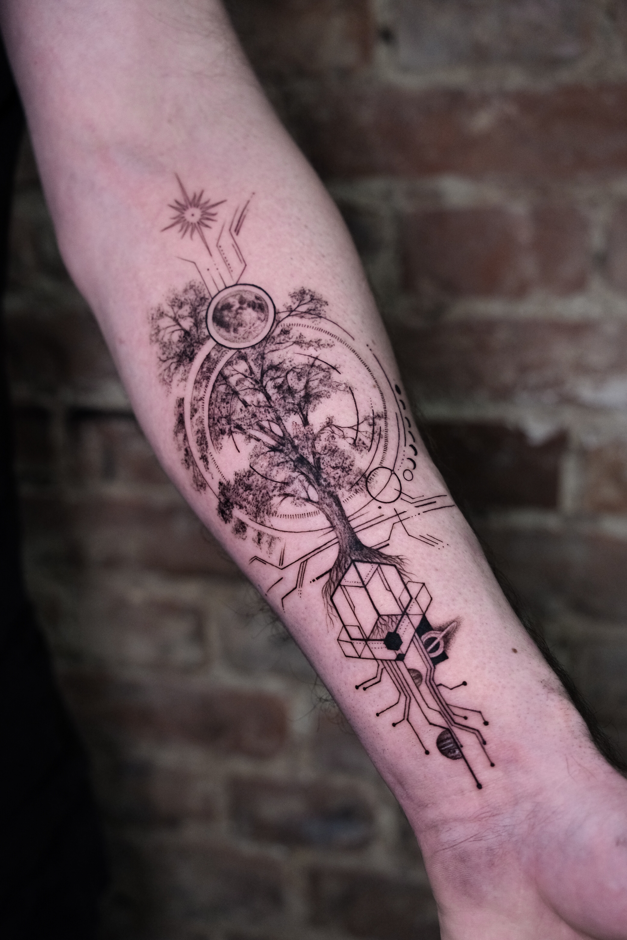 Concept-Tattoo mit Baum, Mond, Sonne und geometrischen Elementen auf dem Unterarm.